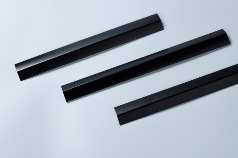 Three identical black metal strips with angled edges are arranged on a light gray background. They appear to be architectural or construction components.