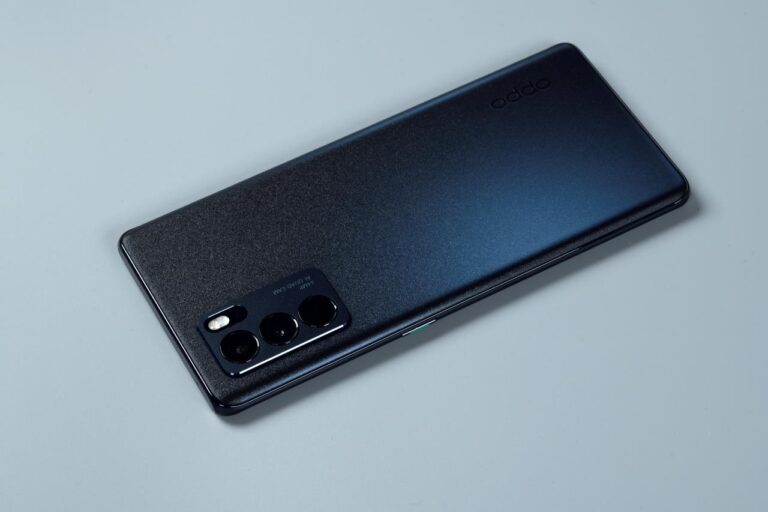 The back of a black Oppo smartphone on a gray background. The phone has a textured finish and a triple-lens camera system.