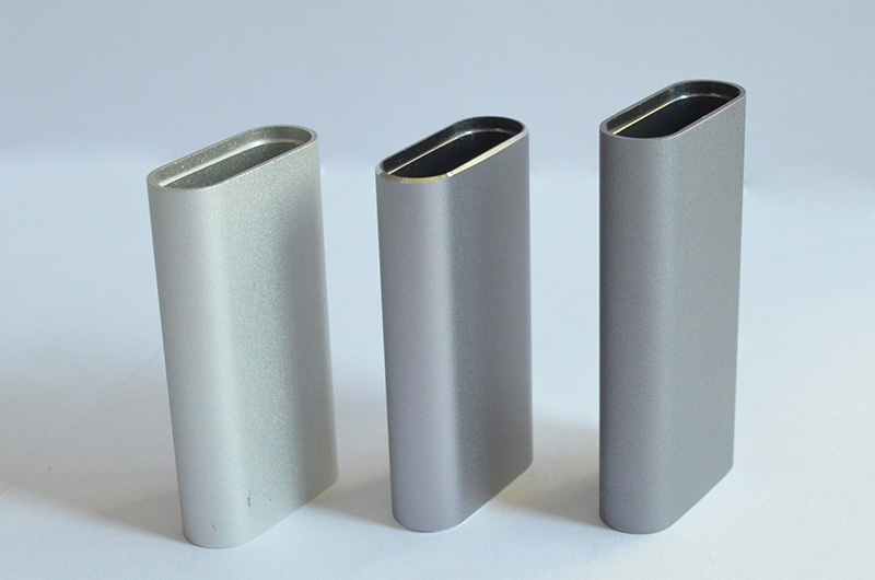 Three oval-shaped metal pieces stand upright on a white background. They appear to be small containers or covers and have slightly different finishes, from light silver to dark gray.